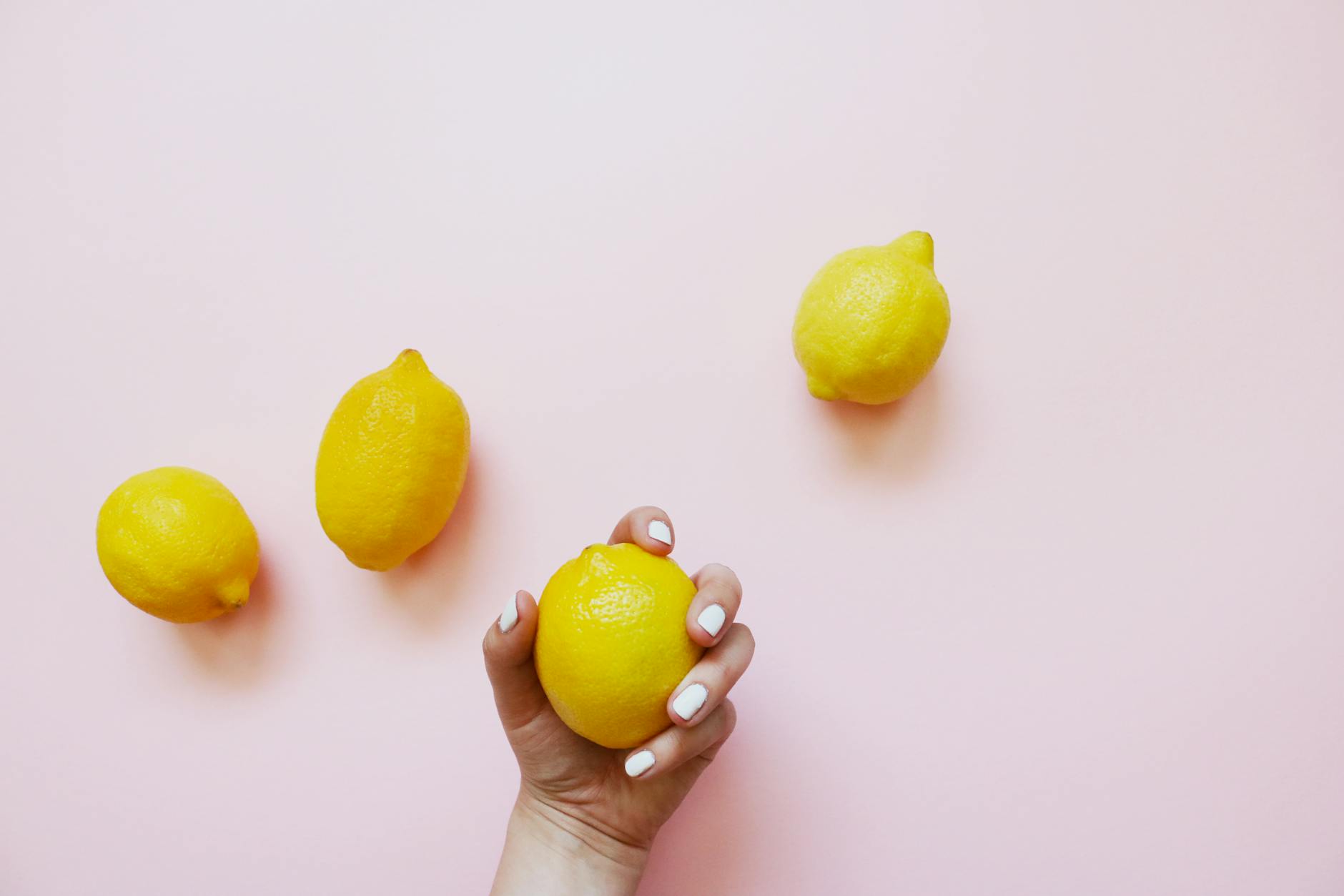 A hand holding a lemon on a soft pink background, symbolizing fresh sensation and vitality