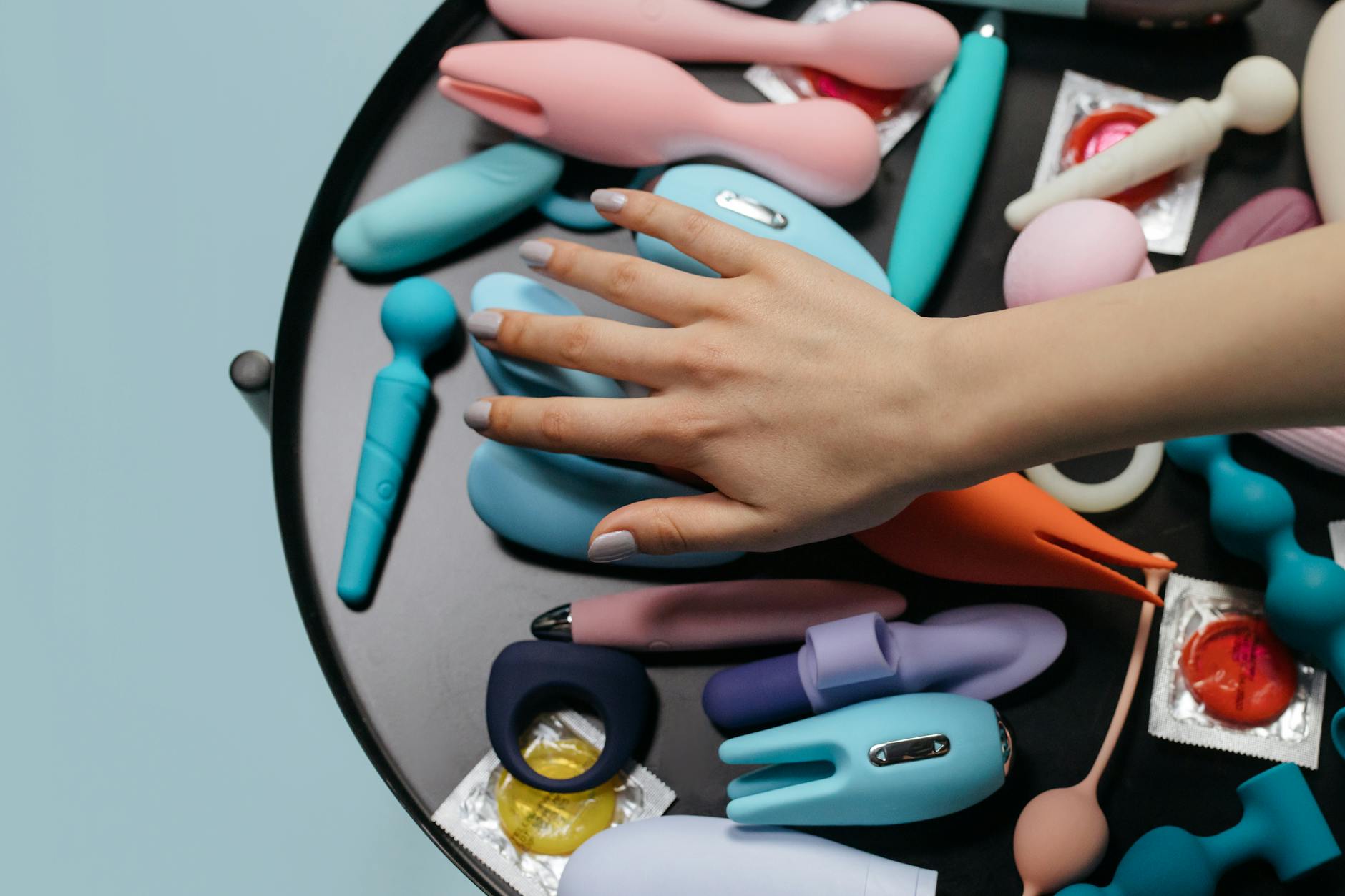 A hand reaching across a variety of clitoral vibrators and adult toys arranged on a table.