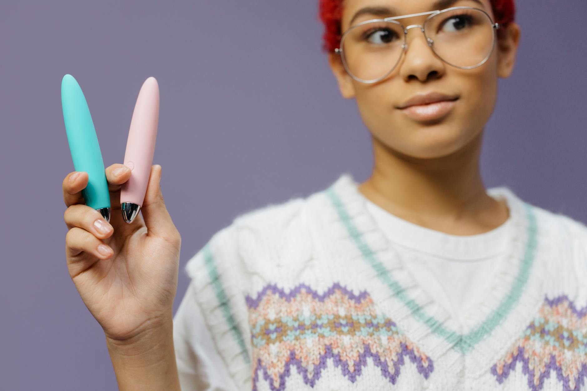 Woman holding colorful vibrators against purple background, representing safe pleasure alternatives