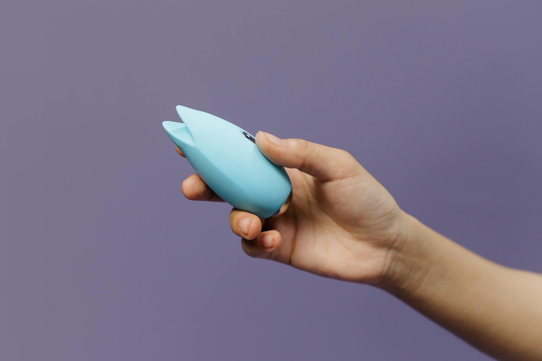 A blue silicone clitoral vibrator held in hand against a purple background, symbolizing personal control and self-pleasure